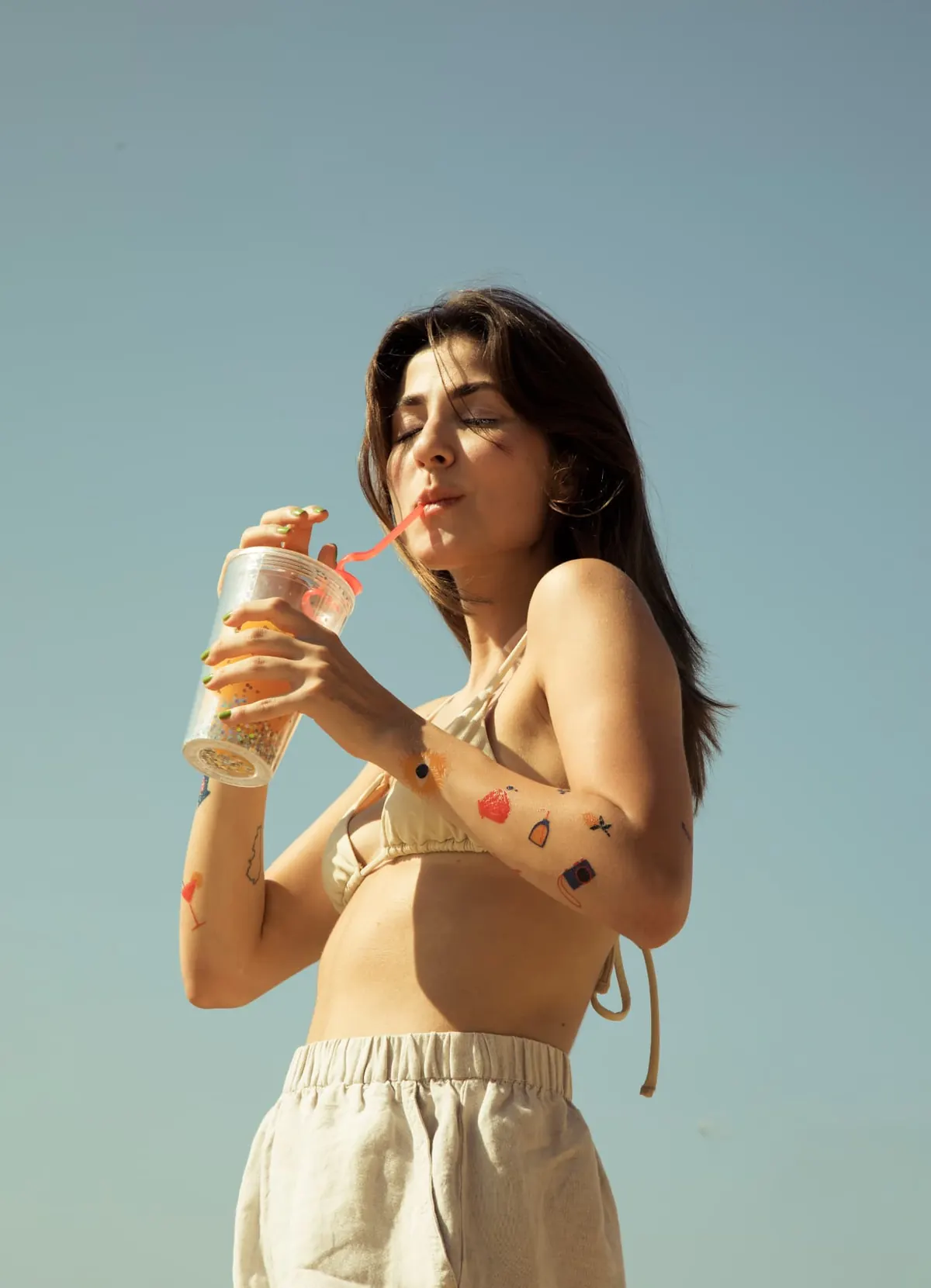Woman wearing colorful temporary tattoos on her arms while holding a drink outdoors